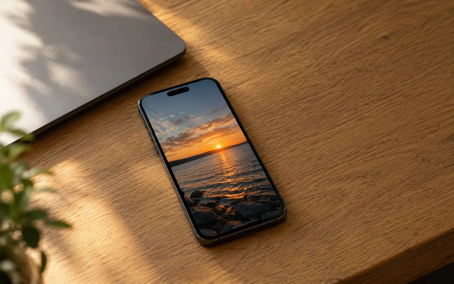 An iPhone on a wooden desk, showing a sunset photo